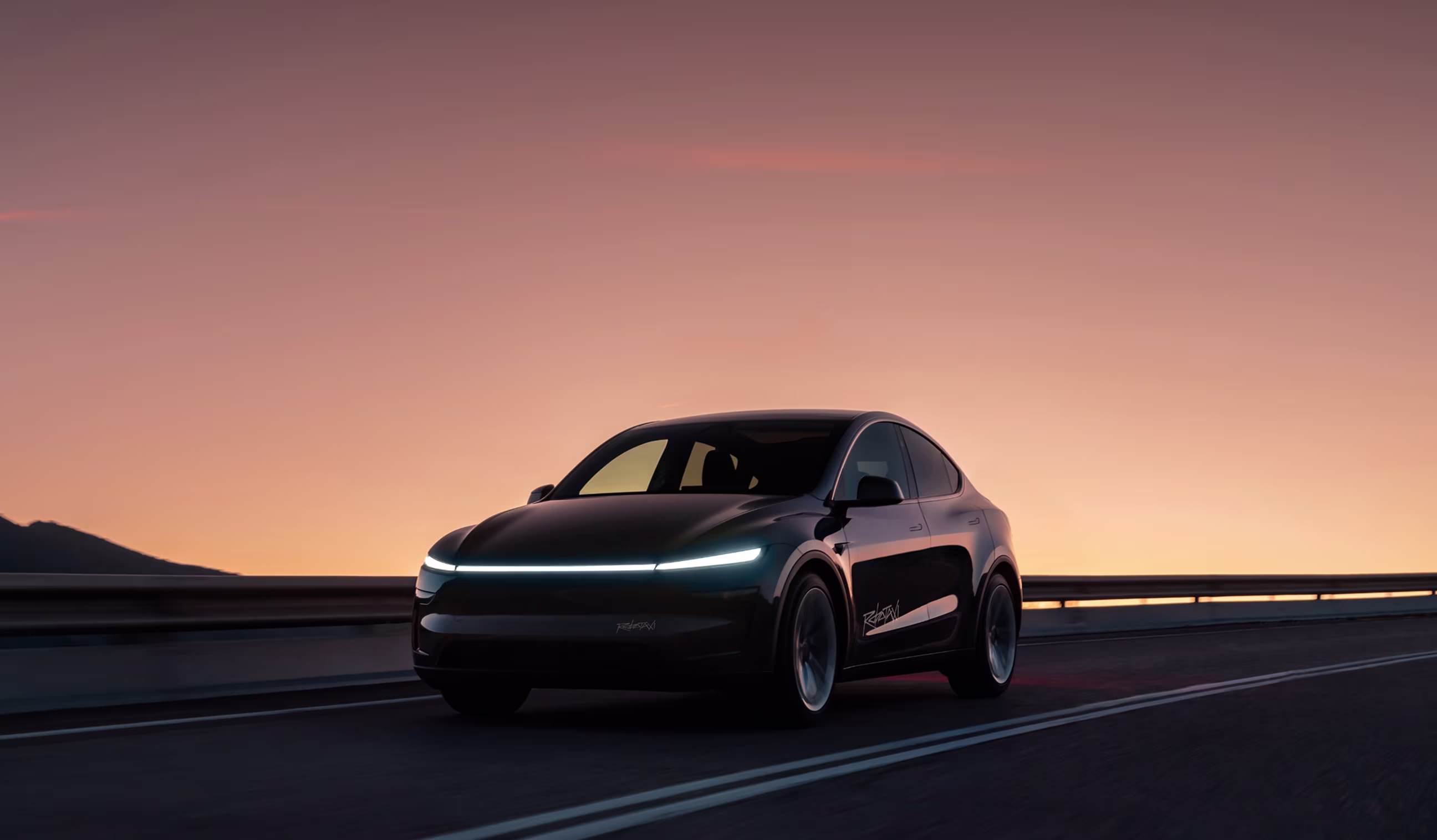 A black Model Y Robotaxi driving on a road at sunset, headlights illuminated, orange and pink sky glowing in the background.